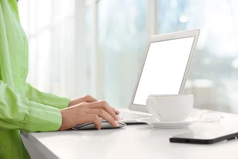 Person using laptop and computer mouse on white desk with coffee cup and smar Stock Photos