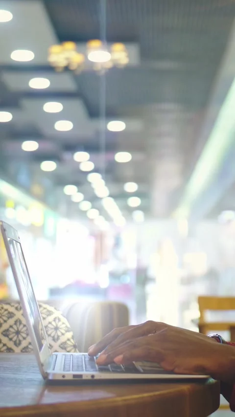 Person using laptop at a cafe table with blurred background and warm ambient Stock Footage 313257338