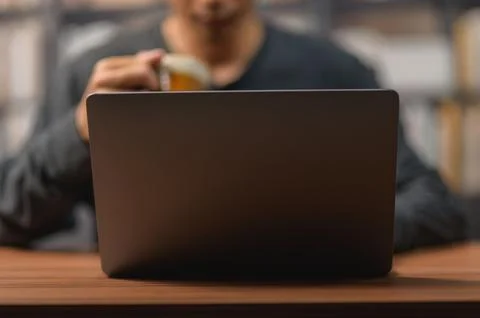 Person Using Laptop Computer and Drinking Coffee in a Cozy Workspace Stock Photos