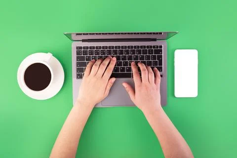 Person using a laptop computer, cup of coffee and smartphone on green backg.. 库存照片