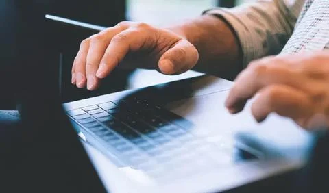 Person using laptop computer at desk in office setting Stock Photos