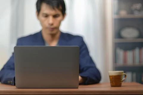 Person Using Laptop Computer at Desk in Home Office with Bookcase and Coffe.. Stock Photos