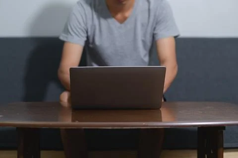 Person Using Laptop on Table in Cozy Living Room Setting Stock Photos