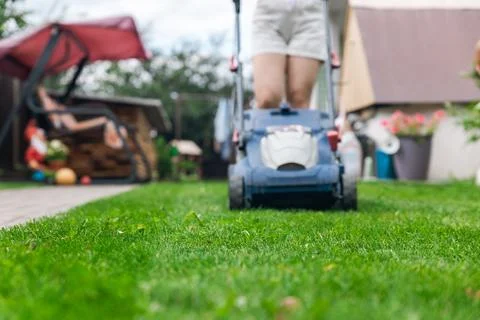 Person using a lawn mower to cut grass in a garden. The mower has a sturdy de Stock Photos