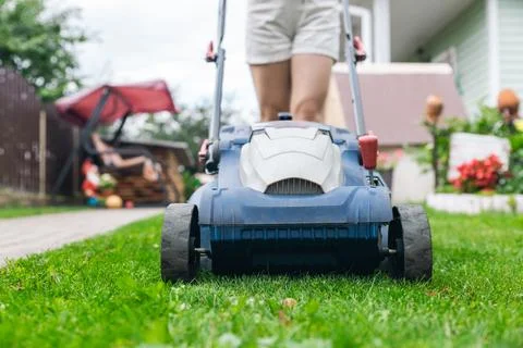 Person using a lawn mower to cut grass in a garden. The mower has a sturdy de Stock Photos