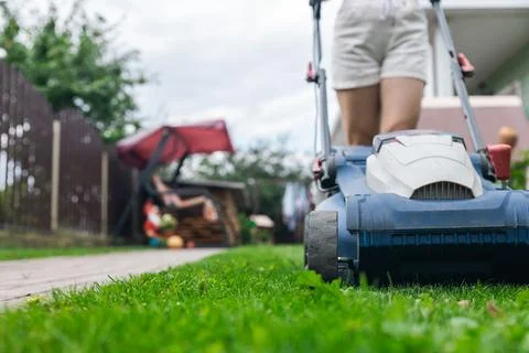 Person using a lawn mower to cut grass in a garden. The mower has a sturdy de Stock Photos