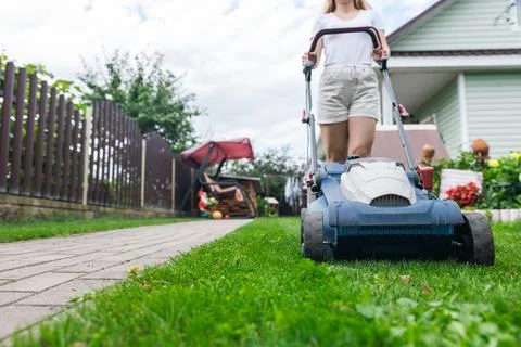 Person using a lawn mower to cut grass in a garden. The mower has a sturdy de Stock Photos