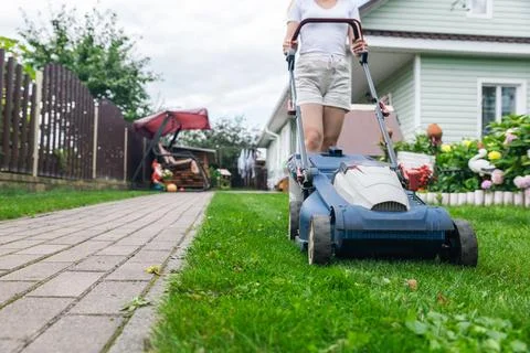 Person using a lawn mower to cut grass in a garden. The mower has a sturdy de Stock Photos