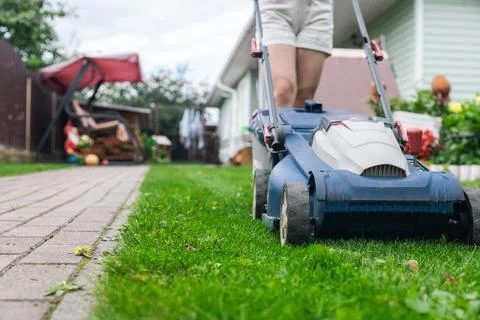 Person using a lawn mower to cut grass in a garden. The mower has a sturdy de Stock Photos