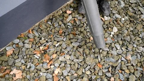 Person using leaf blower to clean fallen brown autumn leaves from grey grav.. Stock Photos