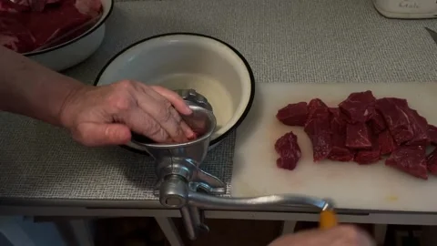 Person using manual meat grinder to mince beef in kitchen setting Stock Footage 344422267