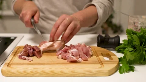 A person is using a meat mallet to tenderize raw pieces of meat on a wooden Stock Footage 336446133