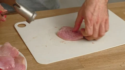 Person using meat tenderizer on raw chicken. Chef preparing pork loin slice with Stock Footage 333464090
