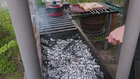 Person Using Metal Poker to Spread Hot Ash Coals in Backyard Barbecue Grill Stock Footage 333822520