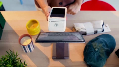 Person using a mobile payment terminal and tablet on a wooden desk point Stock Footage 339159933