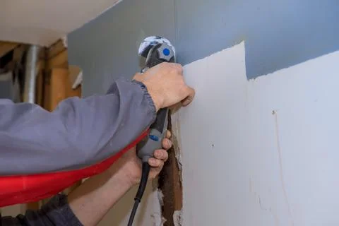 Person using multi tool to cut drywall in home during renovation project Stock Photos