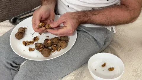 A person using a nutcracker to crack walnuts over a glass bowl on bed Stock Footage 322071532