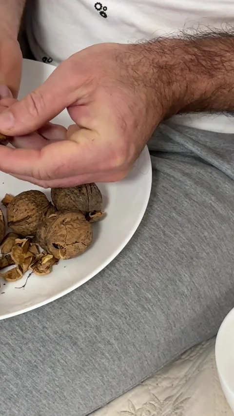 A person using a nutcracker to crack walnuts over a glass bowl on bed Stock Footage 323008244