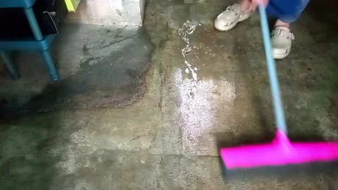 Person using pink squeegee to clear water from concrete floor Video stock 334772379