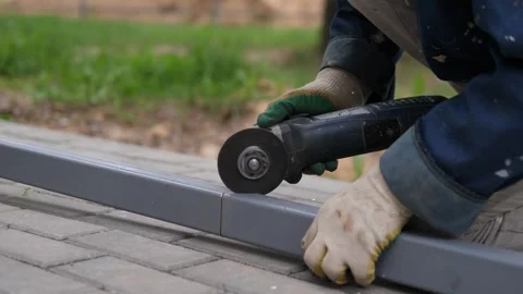 Person using power tool on metal rail in grassy outdoor area with concrete Vídeo Stock 347693364