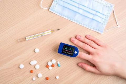 Person using pulse oximeter device near to pills, thermometer and mask Stock Photos