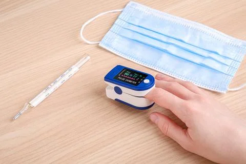 Person using pulse oximeter device near to thermometer and medical mask Stock Photos