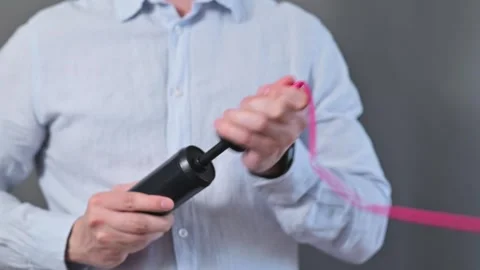 A person is using a pump to inflate a pink balloon in a basic indoor setting. Видео 338300171