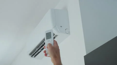 Person using remote control to adjust white wall air conditioner for cooling Stock Footage 336597463
