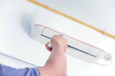 A person using a remote control to adjust an air conditioning unit mounted .. Stock Photos