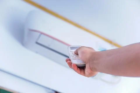 A person using a remote control to adjust an air conditioning unit mounted .. Stock Photos