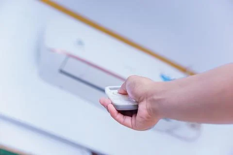 A person using a remote control to adjust an air conditioning unit mounted .. Stock Photos