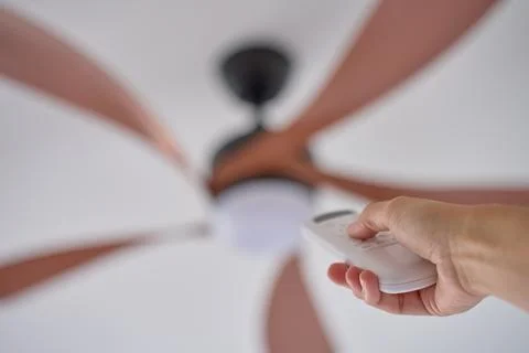 Person using remote control to operate ceiling fan mounted on white ceiling Stock Photos