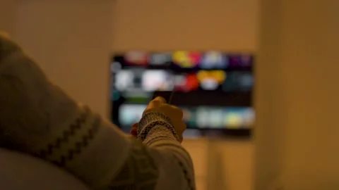 Person Using Remote Control Watching Blurred Tv at Home 動画素材 328352607