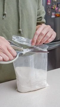 Person using scissors to open a plastic bag containing white powder on a kitchen Stock Photos