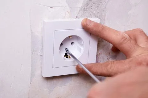 A person is using a screwdriver to install an electrical outlet on a white .. Photos