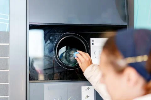 Person using a self-service laundry machine to wash clothes in a modern lau.. Stock Photos