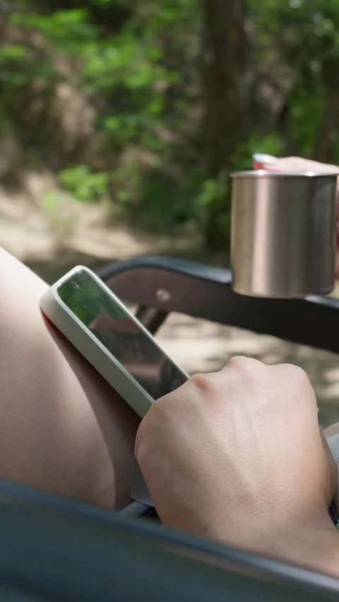 Person Using Smartphone and Holding Metal Mug During Outdoor Camping Stock Footage 341992470