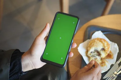 Person using smartphone in cafe while eating cookie Stock Photos