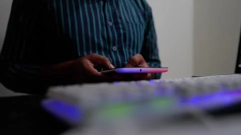Person using a smartphone in a dimly lit room, with a keyboard in the foreg.. Stock Footage 317737401