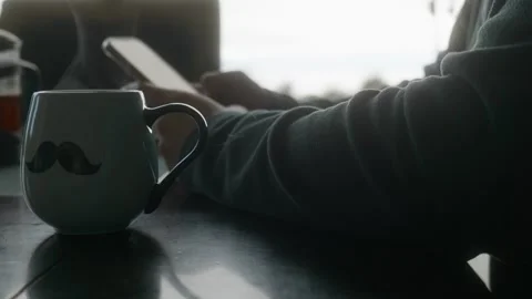 Person using smartphone at dining room table; backlit, only arms in frame Stock Footage 248026861