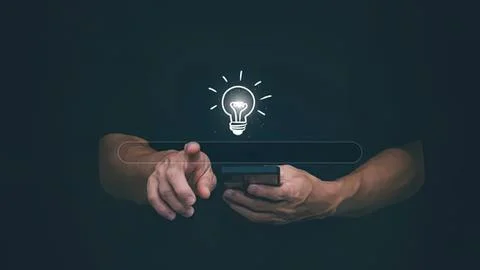 Person using smartphone with glowing light bulb icon Stock Photos