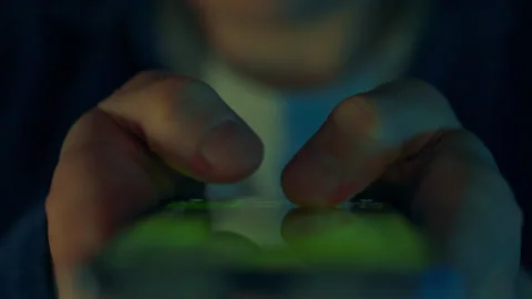 Person using a smartphone in low light focused on the screen during late eve Stock Footage 323708462