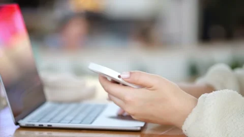 Person using smartphone near open laptop Stock Footage 345706224