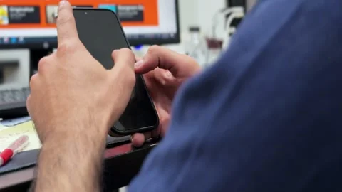 Person Using Smartphone at Office Desk with Computer Screen Background Stock Footage 333443653