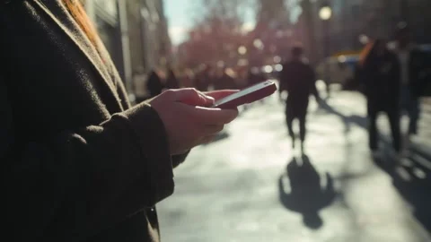 Person using a smartphone outdoors, hands holding the phone, woman walking with Stock Footage 331782446