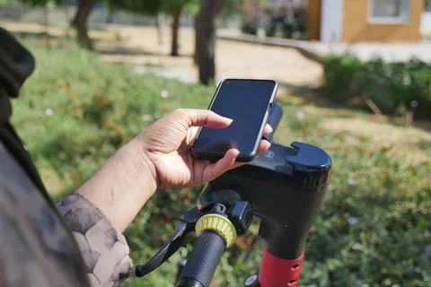 A person using a smartphone to unlock or operate a shared electric scooter via a Stock Photos