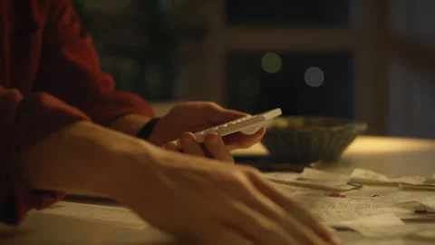 Person using a smartphone while surrounded by paperwork and receipts in a di Stock Footage 323864972