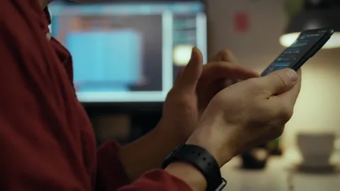 Person using smartphone while working on computer at home office during even Stock Footage 323865049