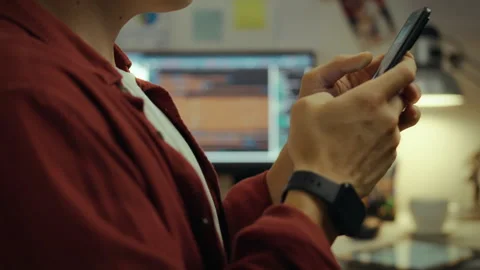 Person using a smartphone while working on a computer in a cozy indoor works Stock Footage 331297397