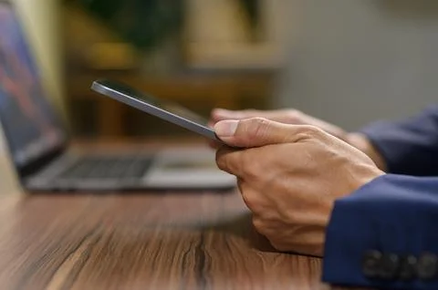 Person Using Smartphone While Working at Desk with Laptop Nearby Stock Photos